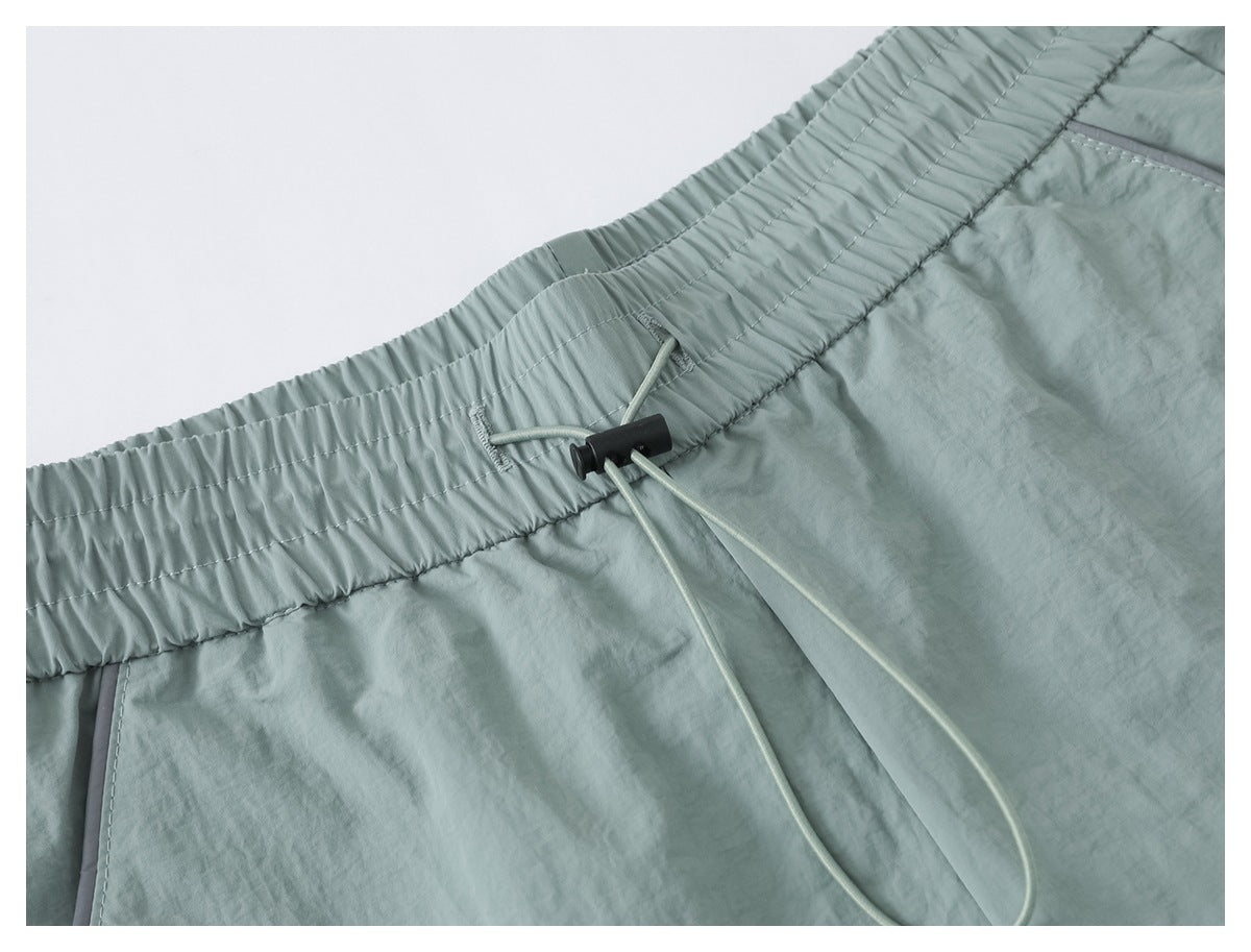 Close-up of sage green pants with a gathered elastic waistband, drawcord, and black cord lock.
