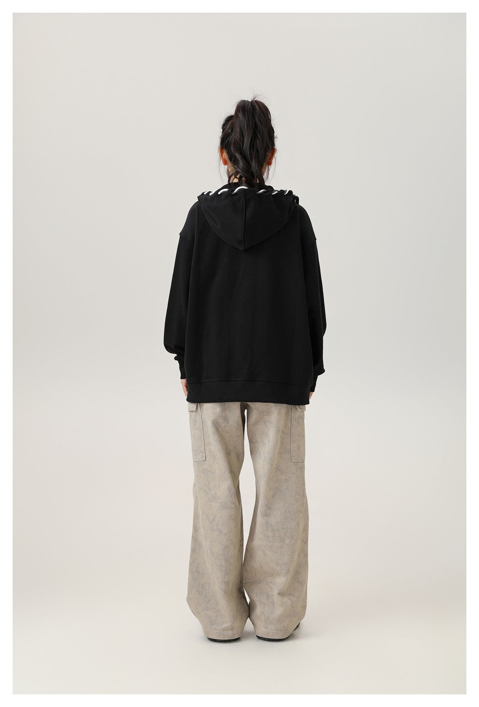 Back view of a model wearing an oversized black hoodie with white cord loops along the hood.