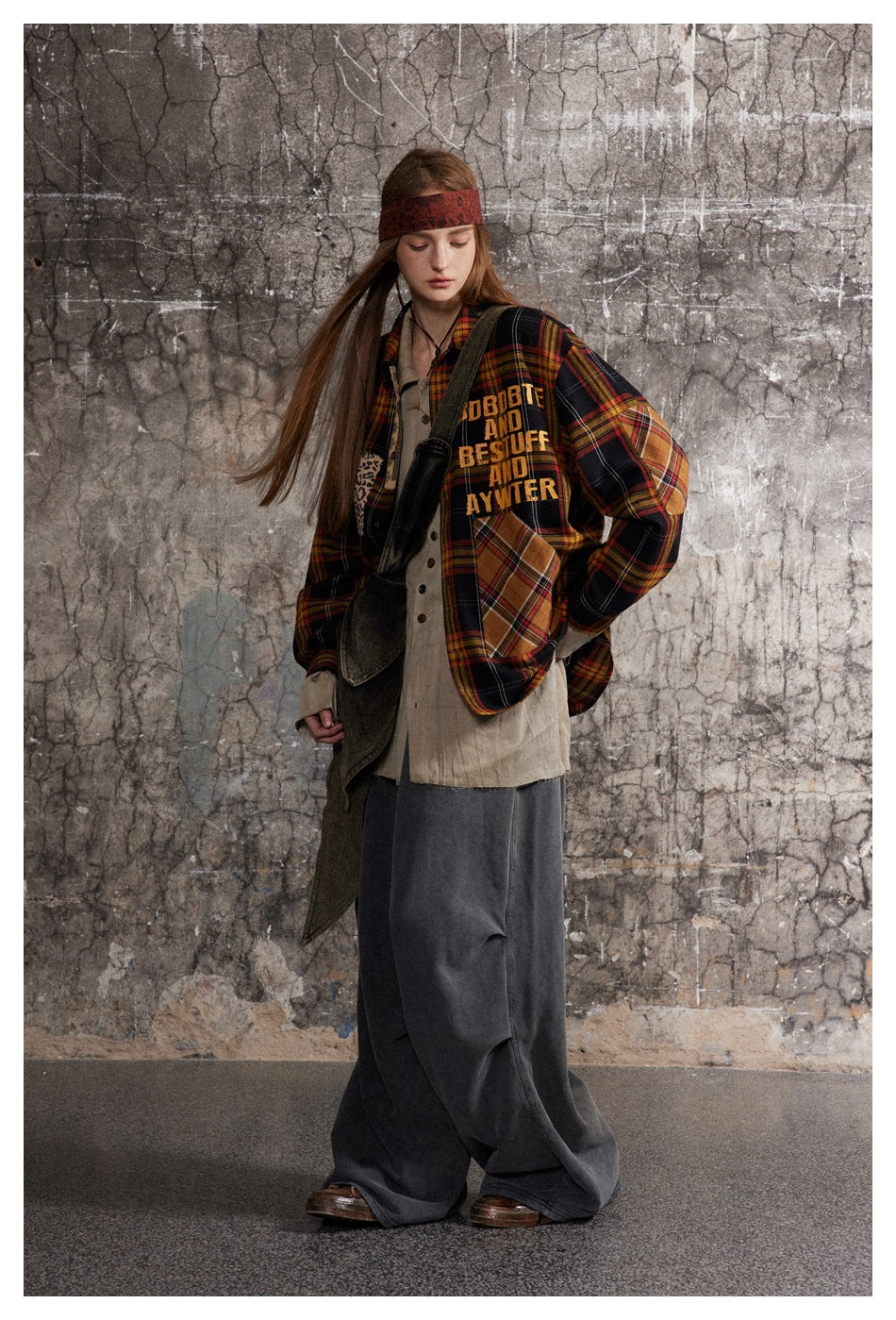 Full-length model wearing a black, red and mustard plaid shirt-jacket with patchwork details and yellow lettering.