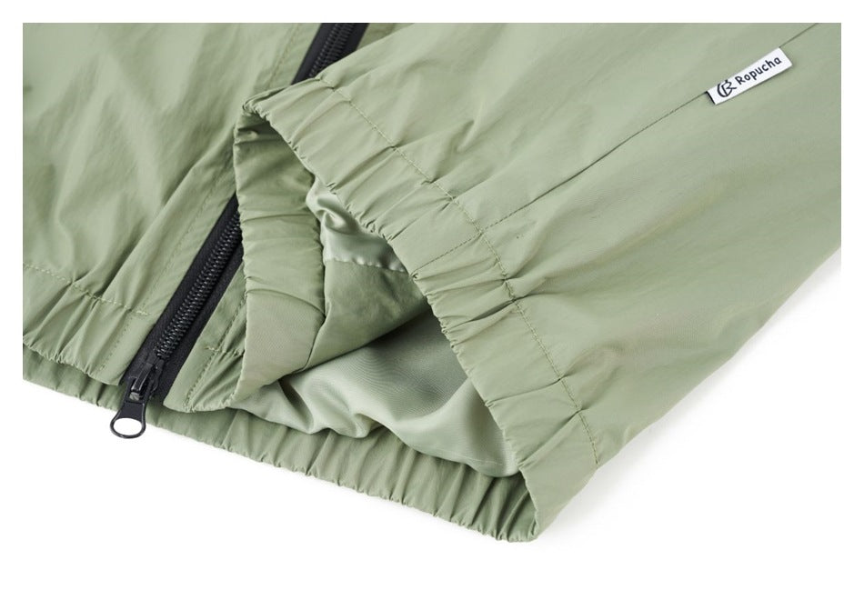 Close-up of the sage green jacket’s gathered hem, black zipper, and small sewn brand label.