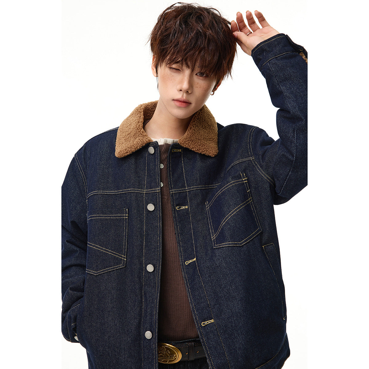 Close view of a model wearing a dark indigo denim jacket with a tan sherpa collar, contrast stitching and two patch pockets.
