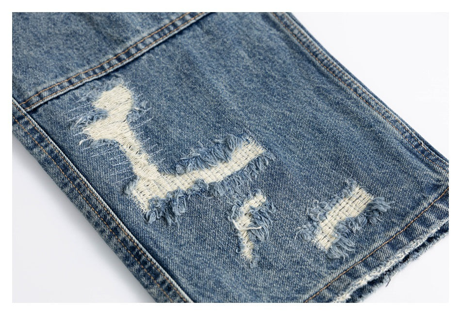 Close-up of blue denim with several frayed, light-colored distressed patches and visible seams.