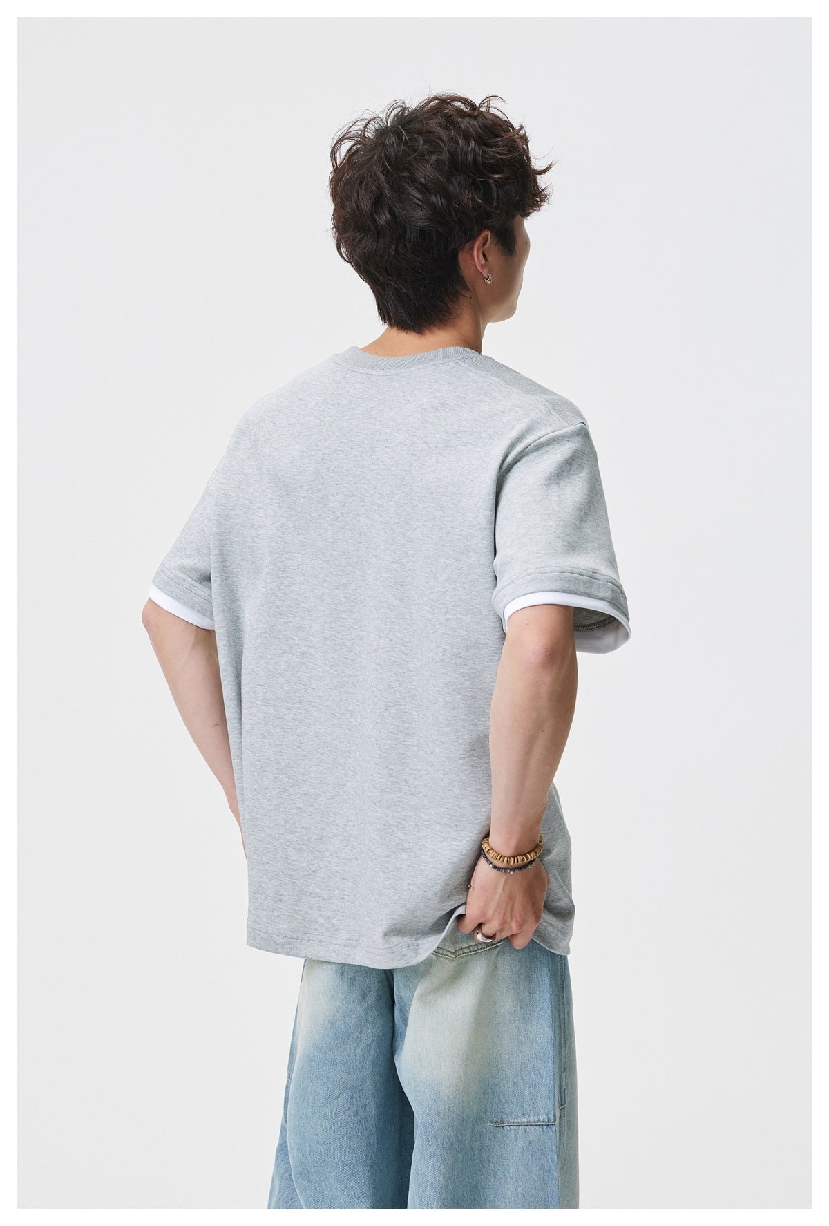 Rear view of a model wearing a plain oversized light gray tee with white sleeve trim.