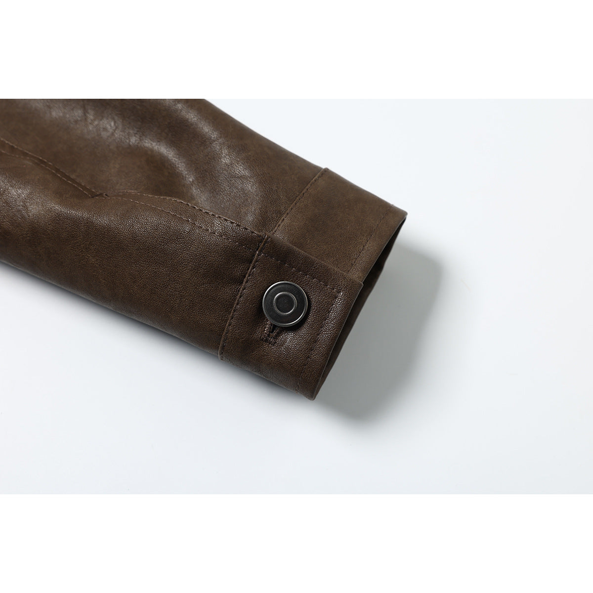 Close-up of a dark brown jacket sleeve cuff with a round metal snap and stitched seams.