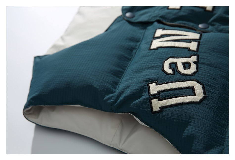 Close-up of the vest's dark teal front, cream appliqué lettering, snap placket, and cream lining.