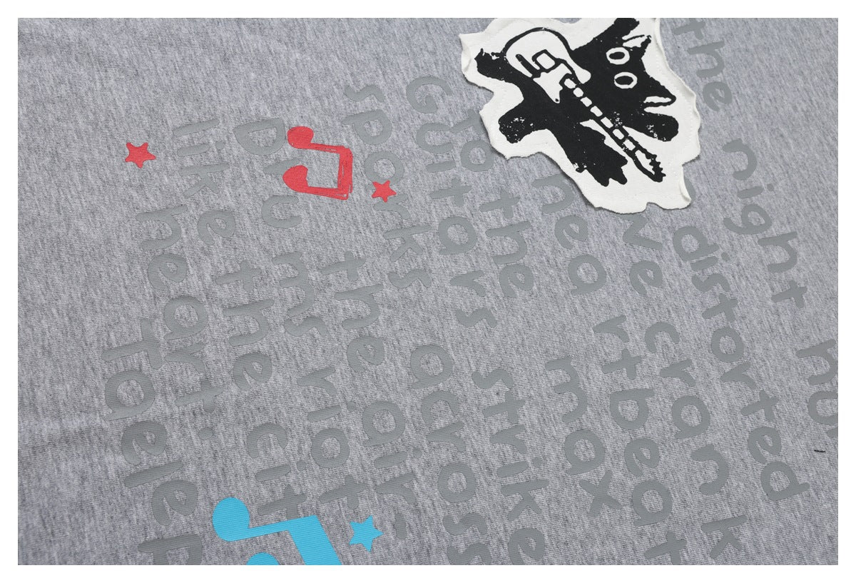 Close-up of a gray garment with large gray lettering, red and blue accents, and a black-and-white graphic print.