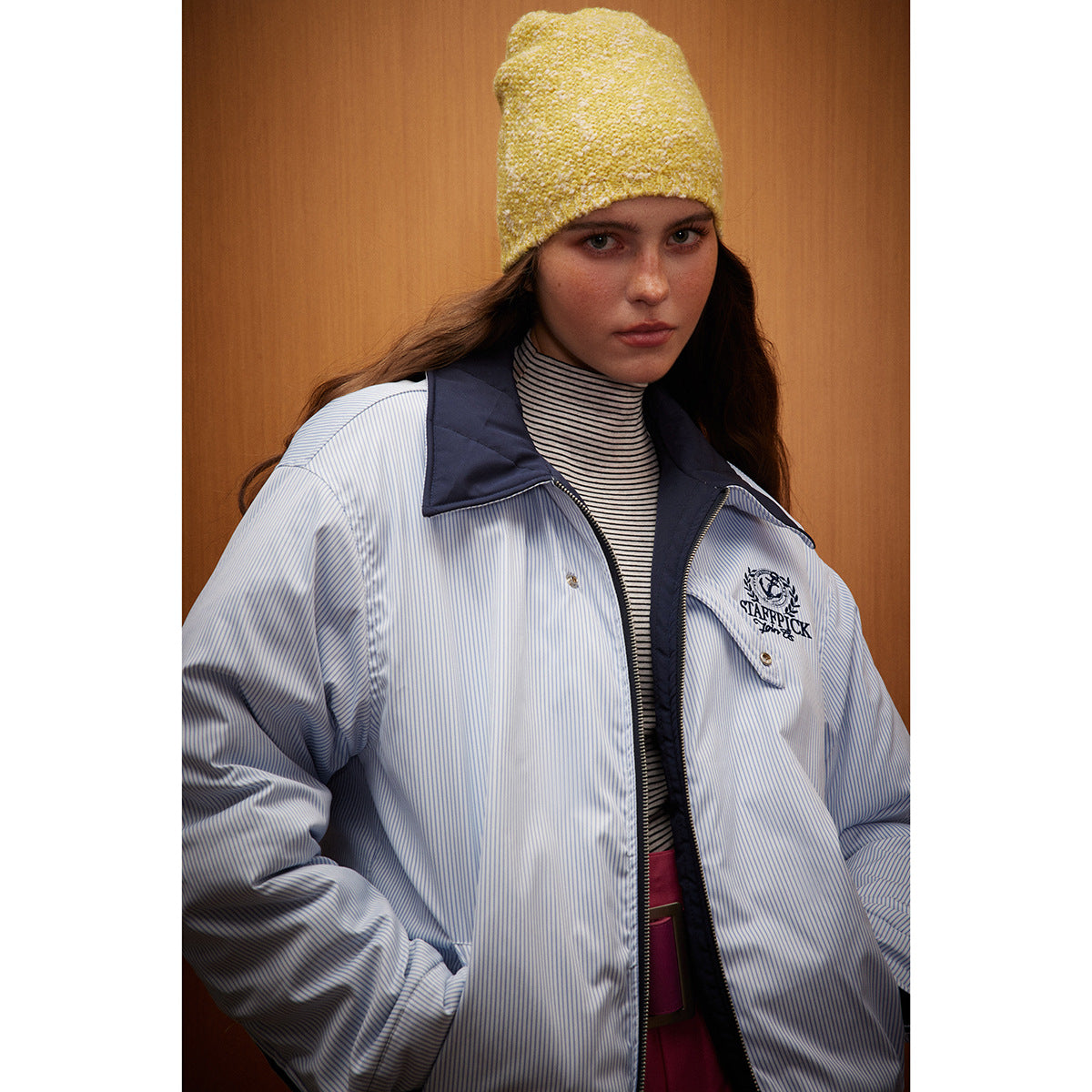 Close view of a model in a light blue pinstriped jacket with a navy collar and embroidered crest, wearing a yellow knit