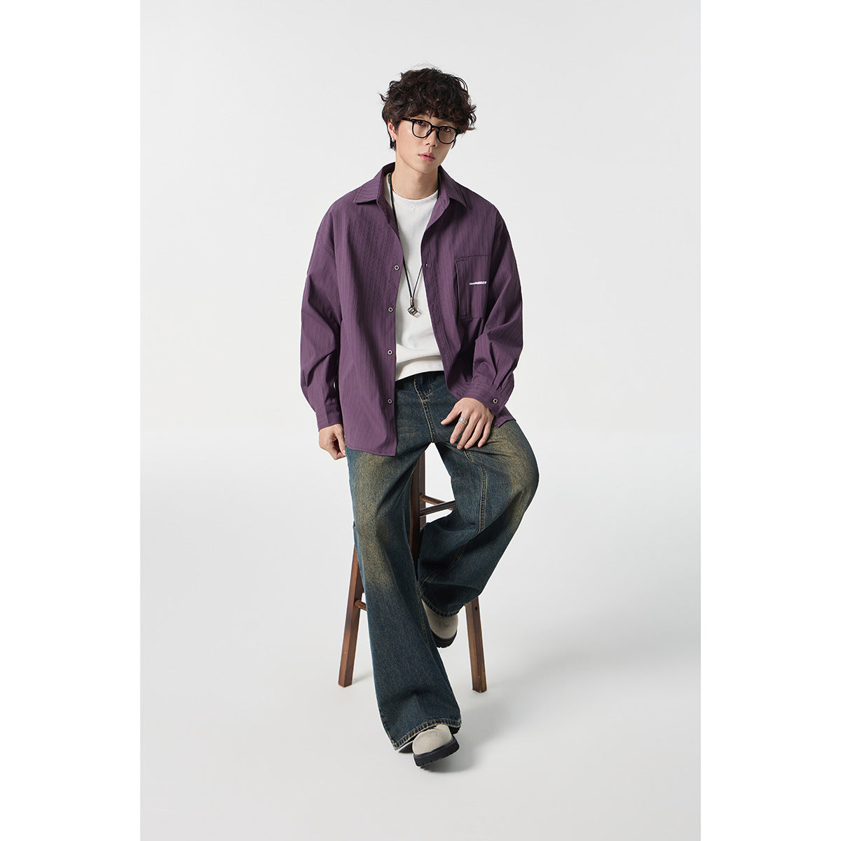 Seated model wearing a plum button-up shirt over a white tee with loose, faded jeans.