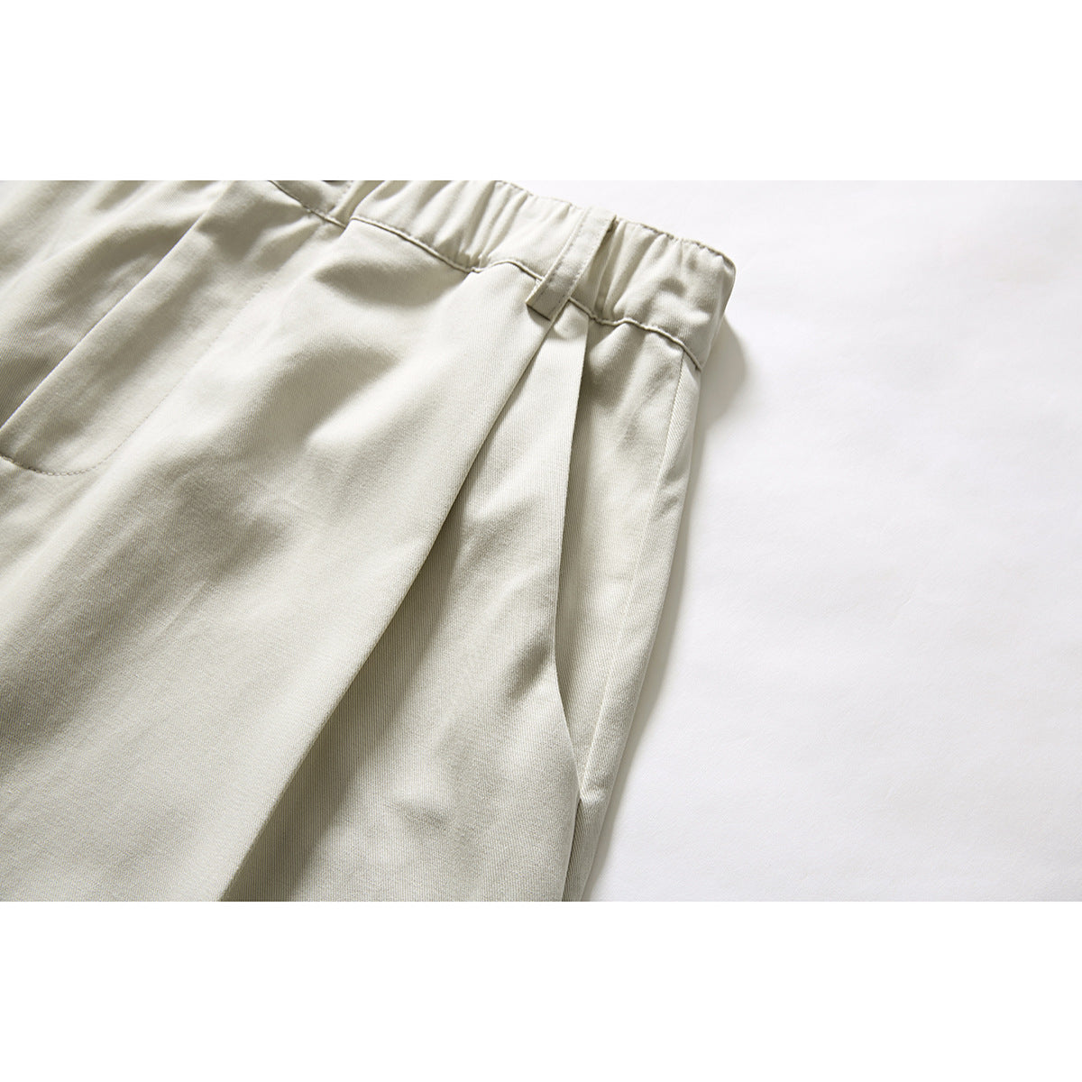 Close-up of cream shorts showing a belt loop, waistband and side pocket opening.