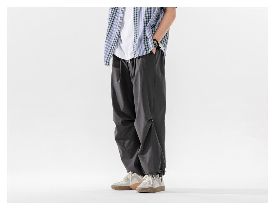 Model wearing charcoal wide-leg pants with gathered cuffs, paired with a white shirt and an open plaid shirt.