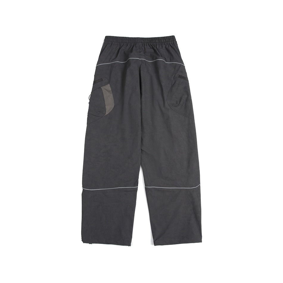 Back view of loose charcoal cargo pants with curved pockets and light piping across the seat and lower legs.