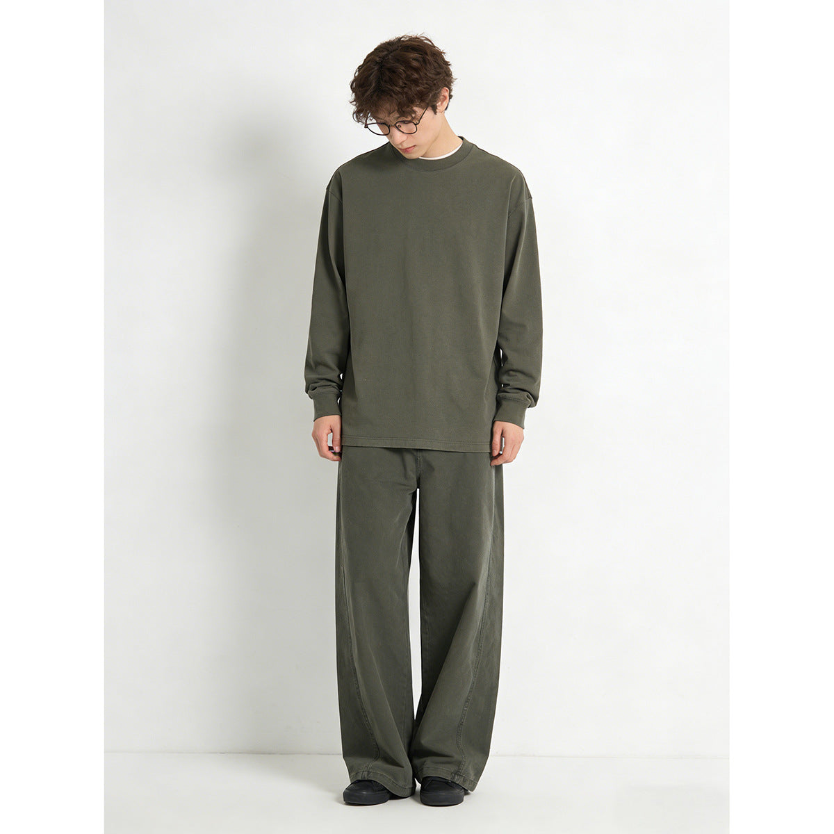 Model wearing a dark olive long-sleeve crewneck top with matching loose trousers, shown full length.