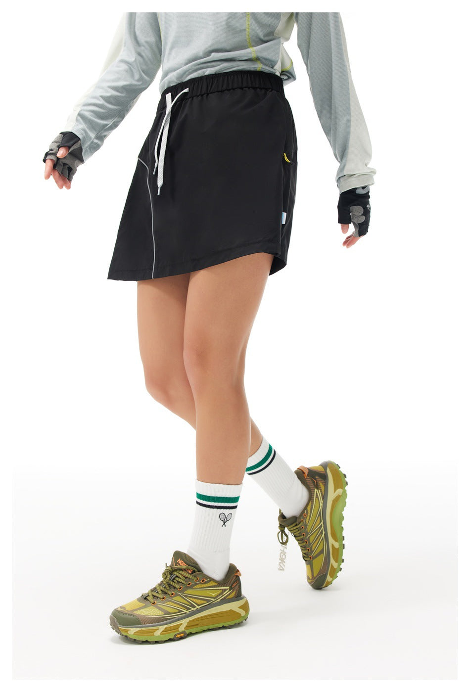 Model wearing a black athletic skort with an elastic waist, white drawcord, and curved seam detail.