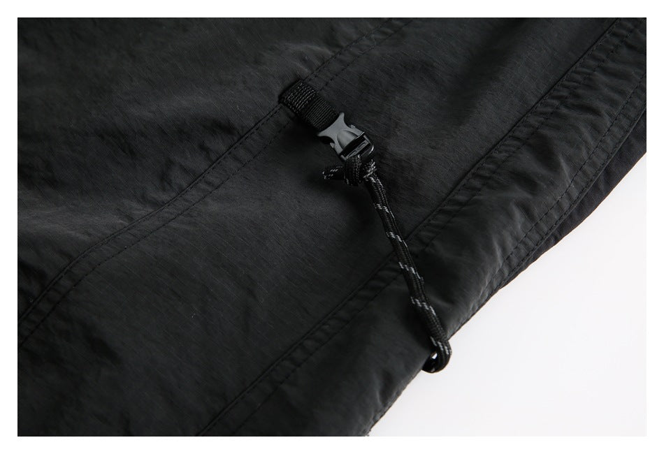 Black garment detail showing a cord lock, adjustable cord, and stitched panel seams.