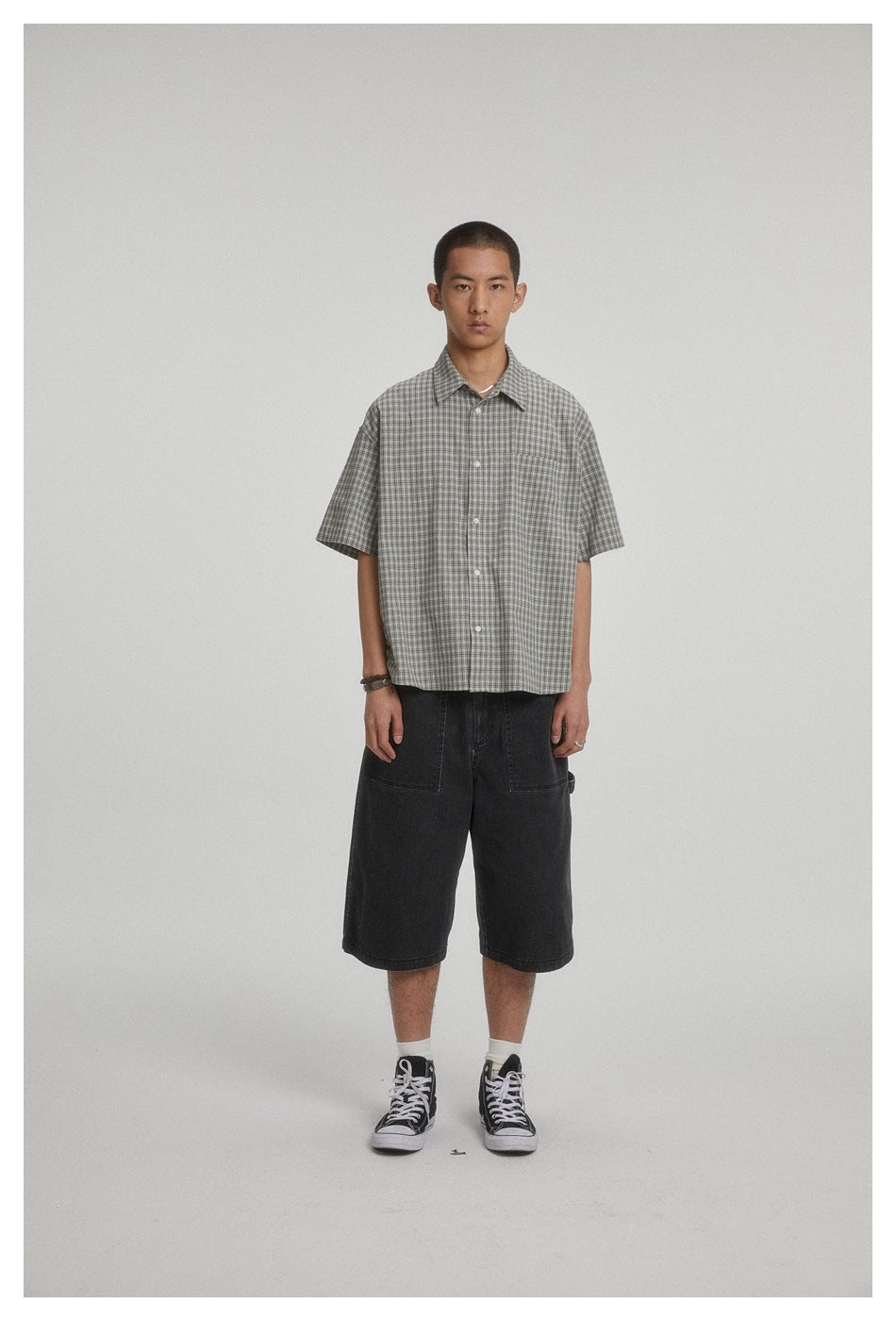 Front view of a model wearing a relaxed gray plaid short-sleeve button-up shirt with a chest pocket.