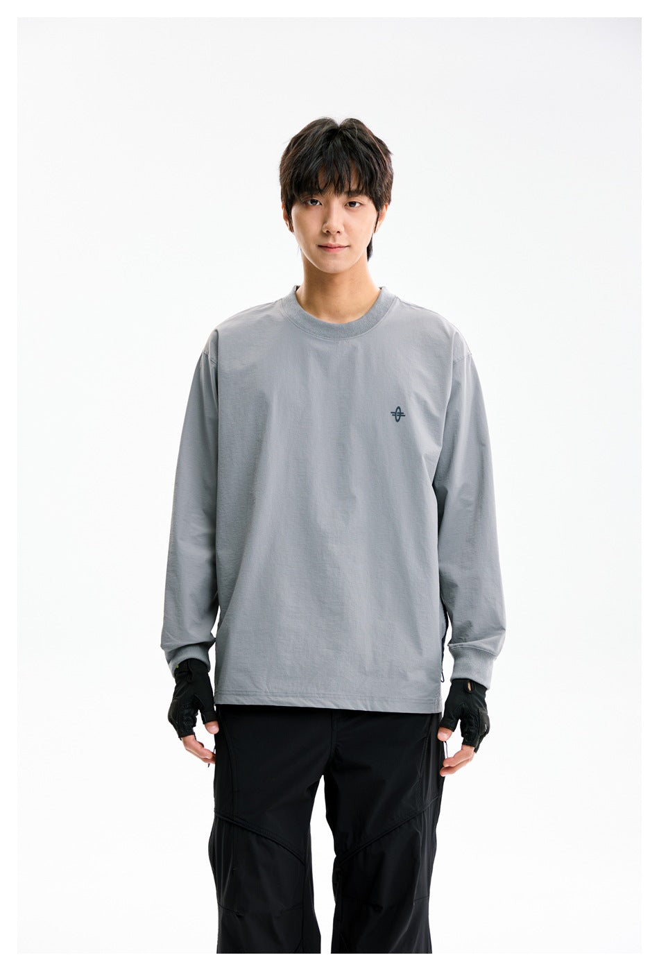 Model wearing a loose gray long-sleeve crewneck shirt with a small dark chest emblem and black pants.