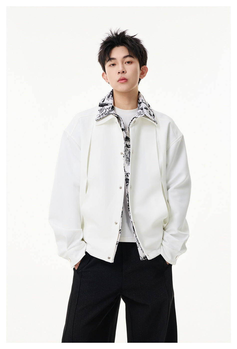 Front view of a model wearing a white jacket with botanical print details over black trousers.