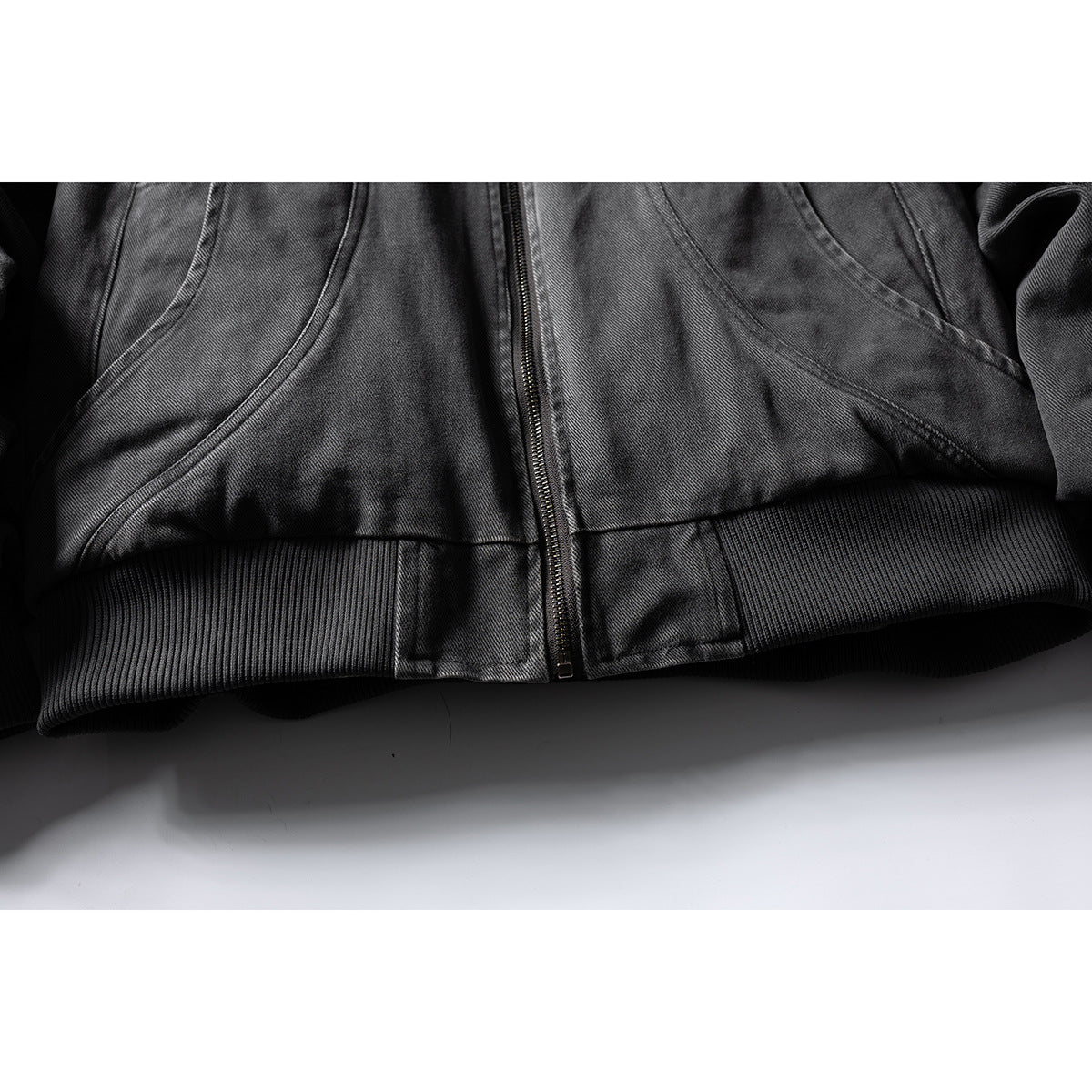 Close-up of the dark gray jacket's front zipper and wide black ribbed hem.