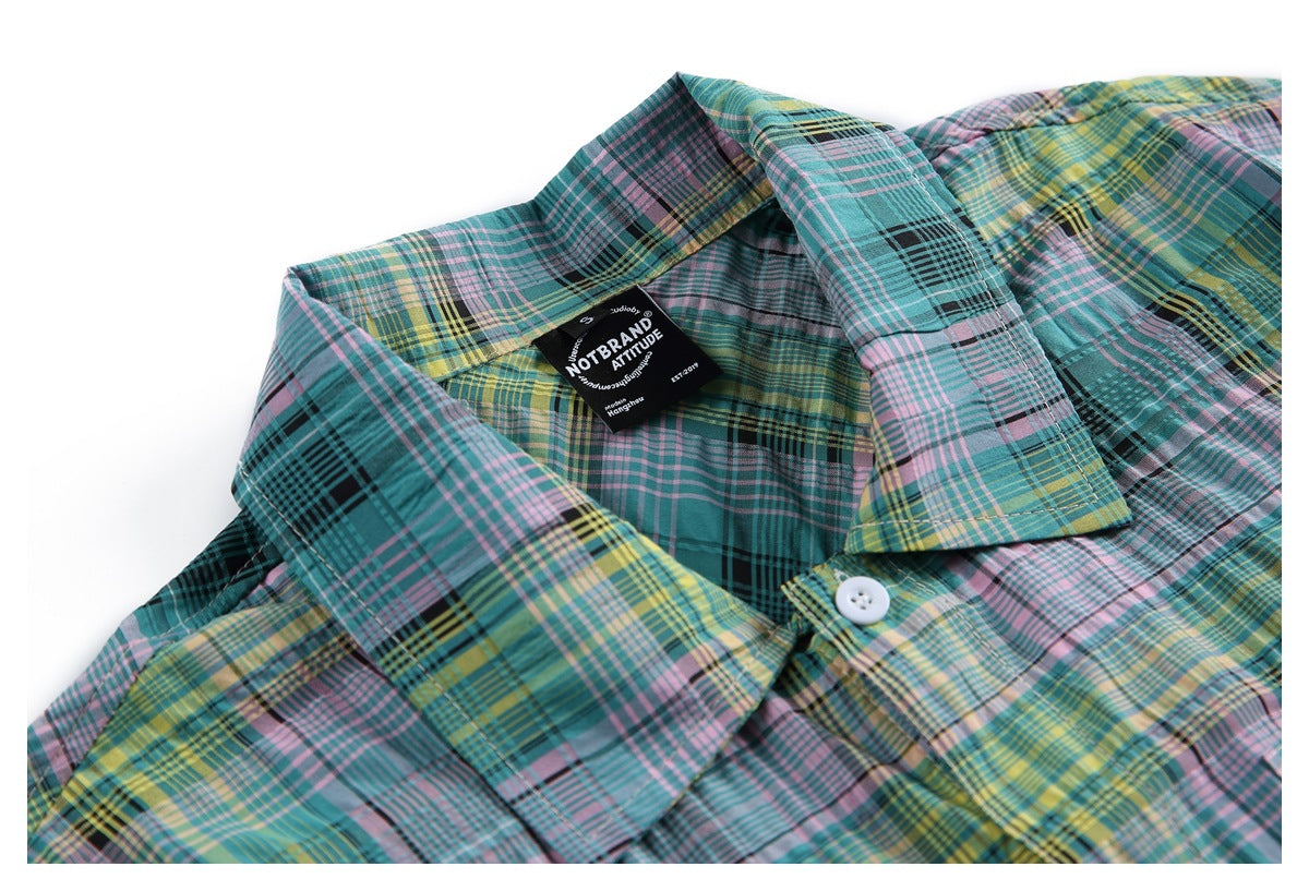 Close-up of a teal plaid shirt collar, white button, and black neck label.