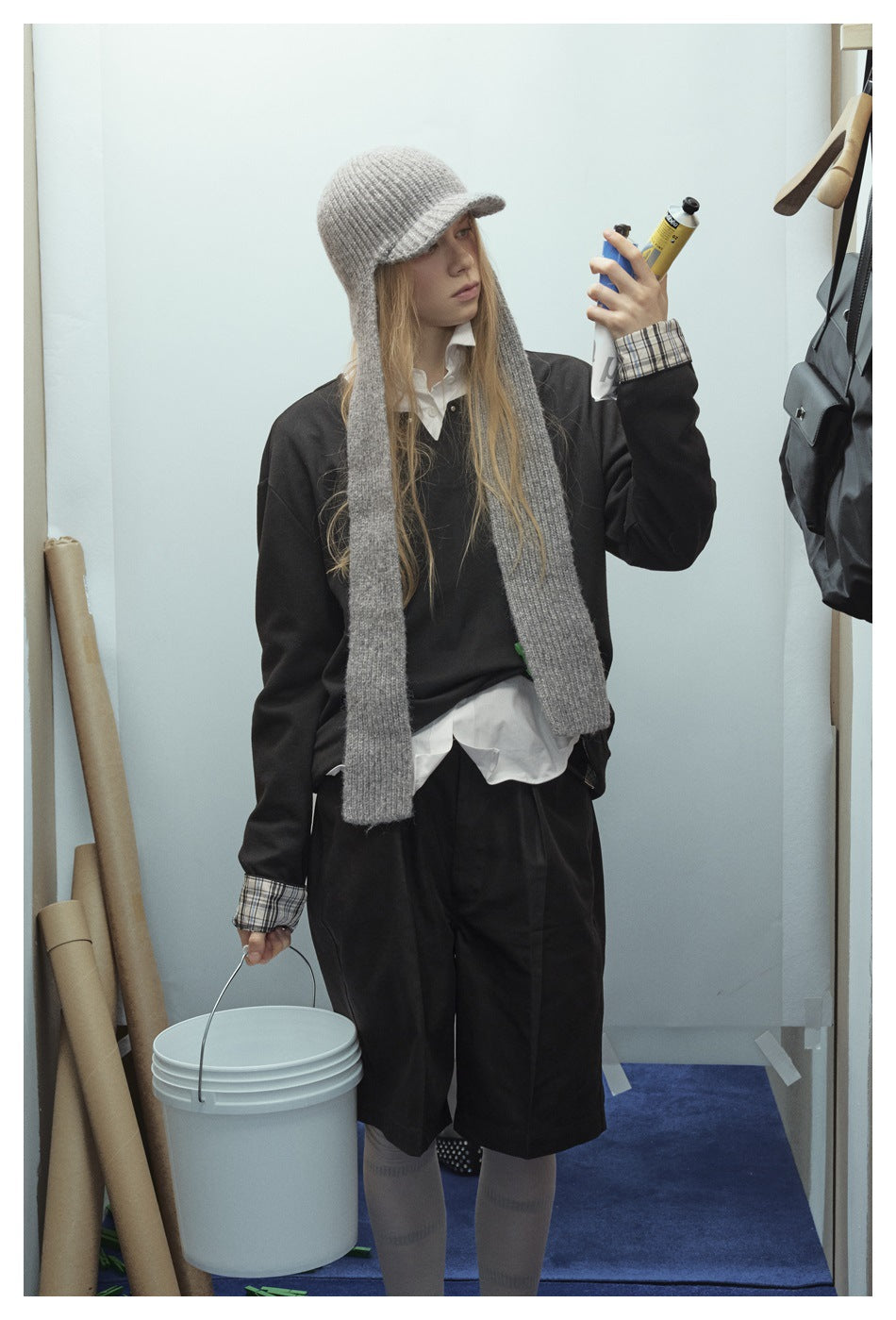 Three-quarter view of a model wearing a black top and shorts with plaid cuffs, a white shirt, and a long gray scarf.
