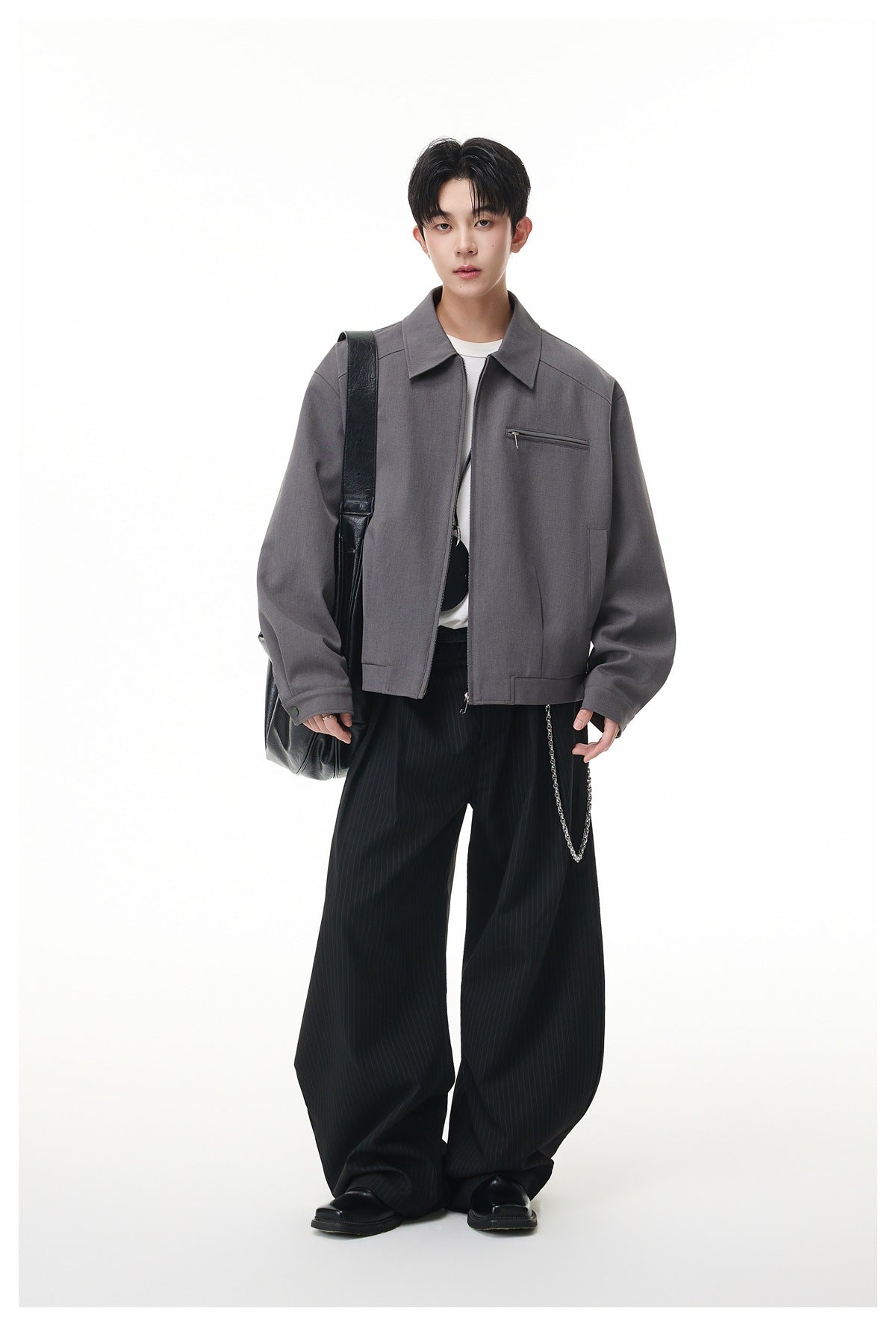 Model wearing gray zip jacket over a white tee with black pinstripe wide-leg pants and a black shoulder bag