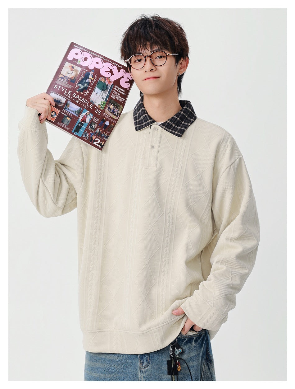 Model wearing an ivory patterned pullover with a dark plaid collar and holding an open magazine.