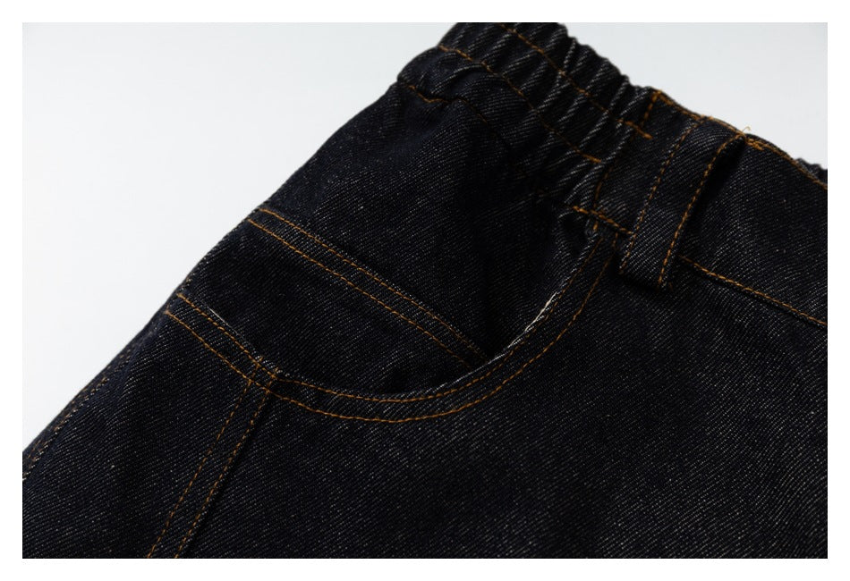 Close-up of black denim pants showing an elastic waistband, belt loop, curved pocket, and orange-brown stitching.