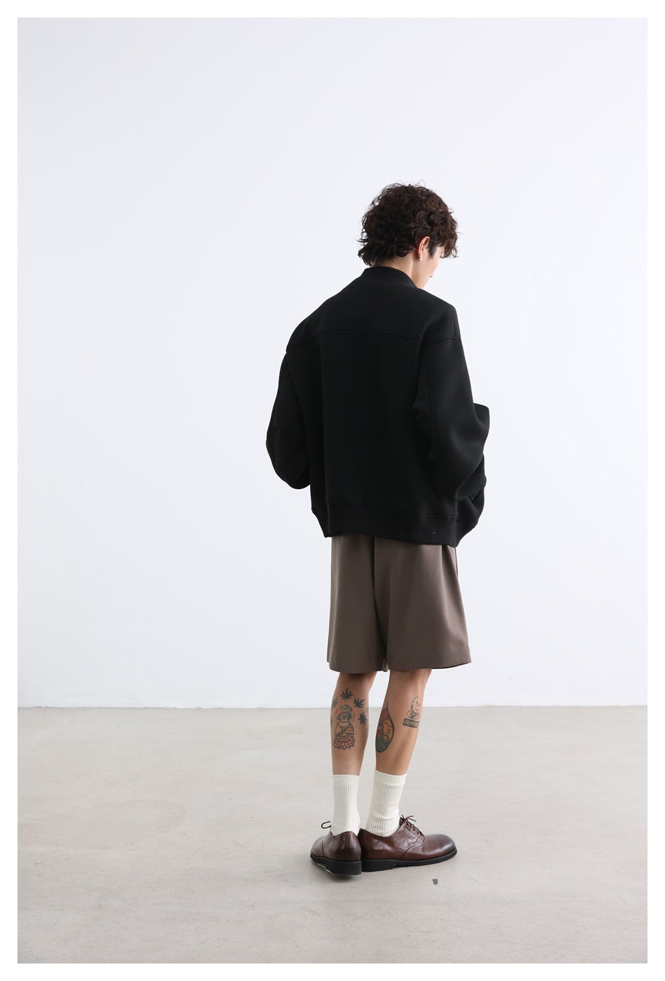 Model wearing a black jacket and taupe shorts, shown from the back.