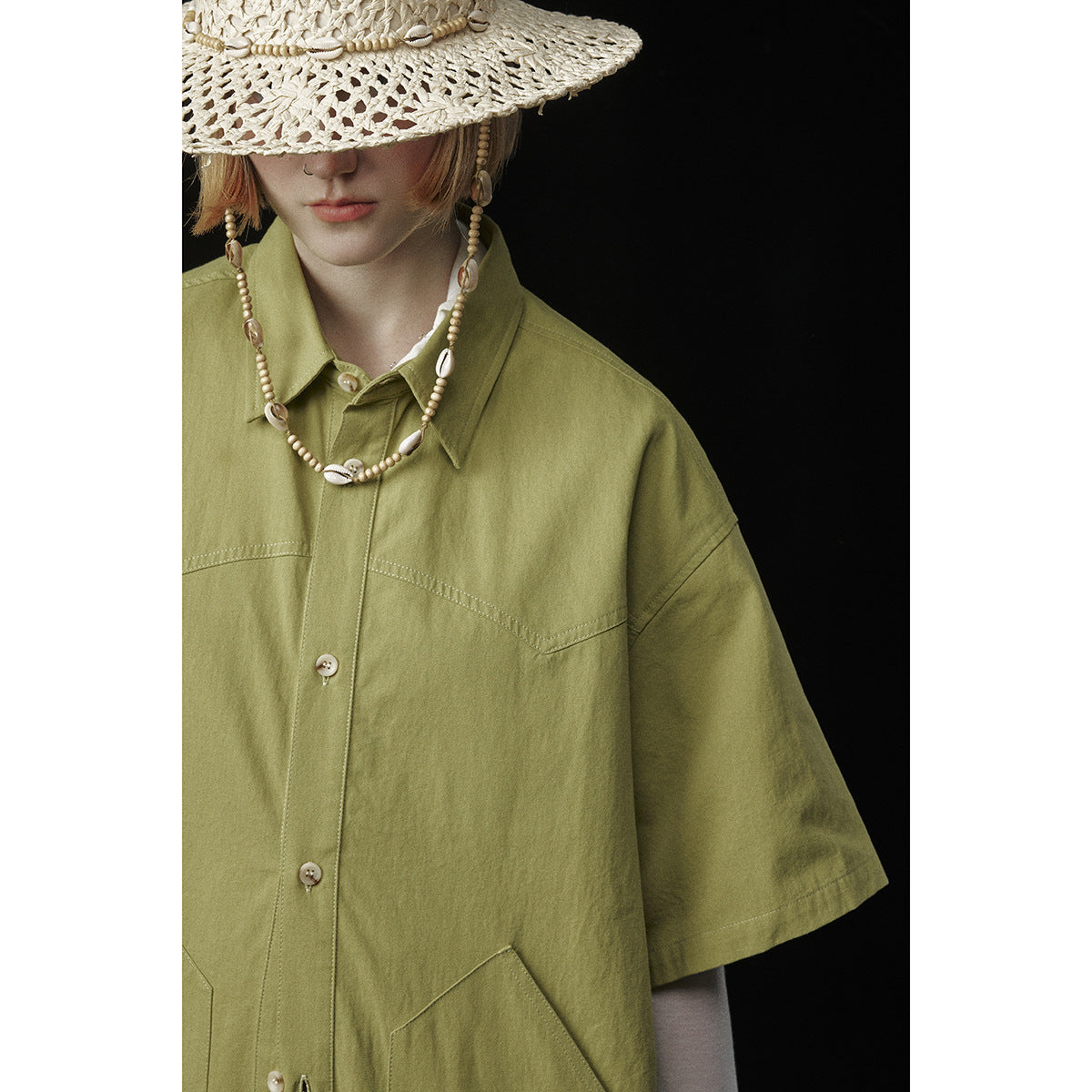 Close view of an olive-green short-sleeve button-up shirt with contrasting topstitching and large pockets.