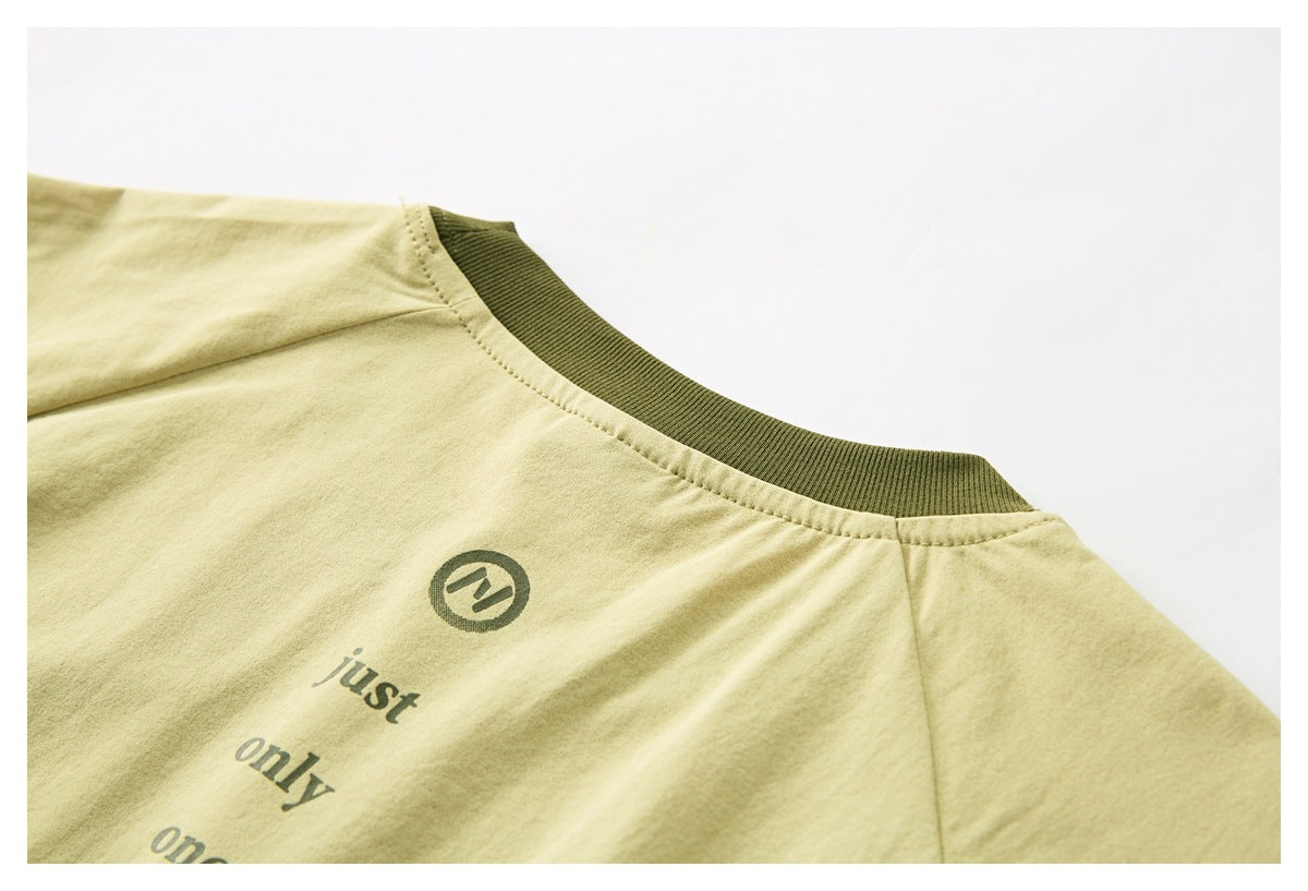 Close-up of a pale yellow T-shirt with an olive ribbed collar and part of a dark printed text graphic.