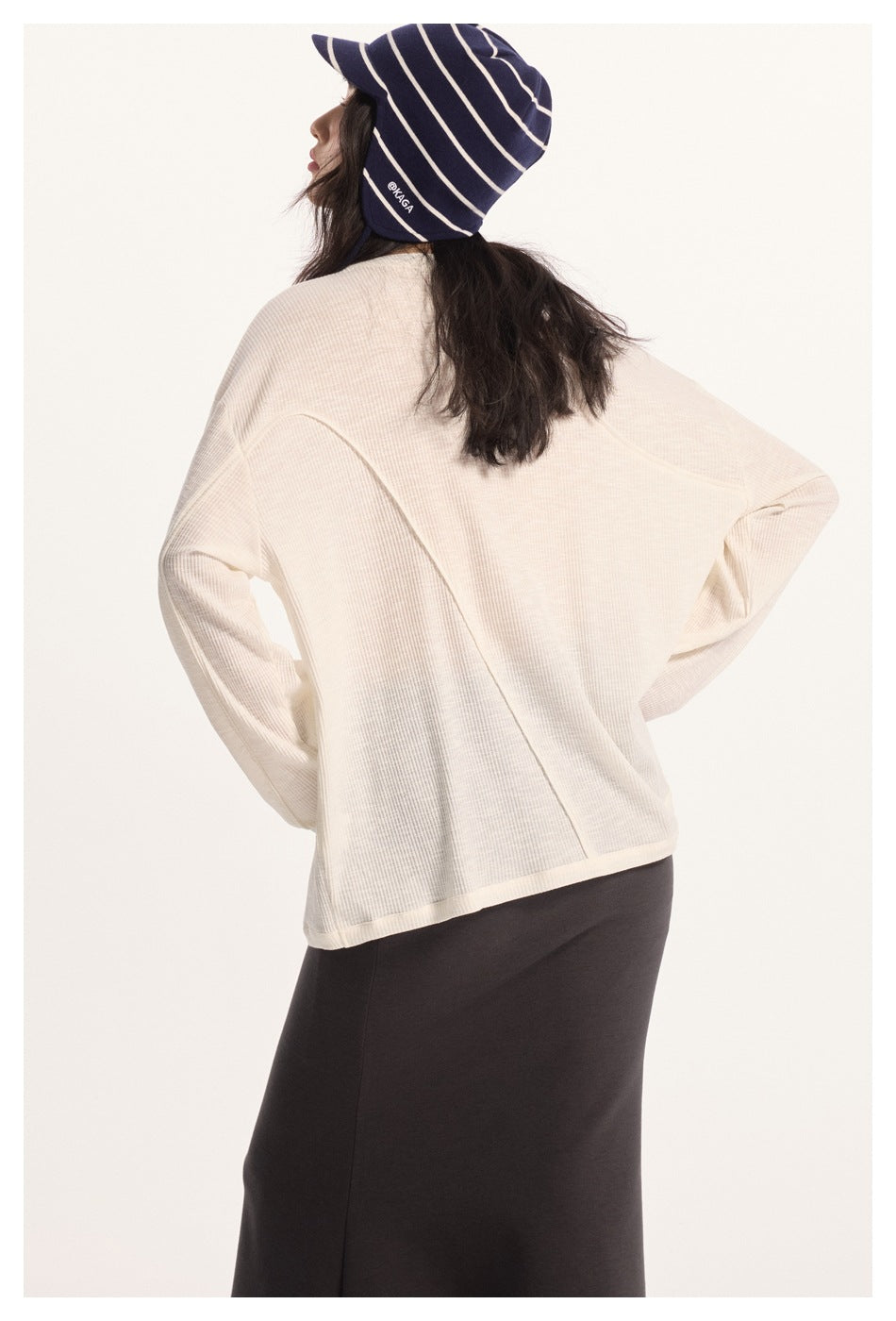 Rear view of a model wearing a cream ribbed top with curved seams and a navy striped hat.