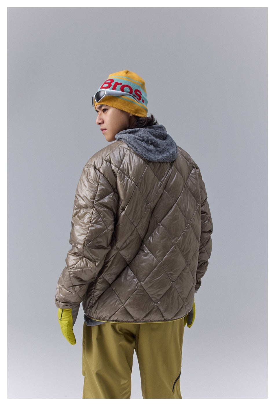 Rear view of a taupe quilted jacket with diamond stitching and a gray hood worn by a model.