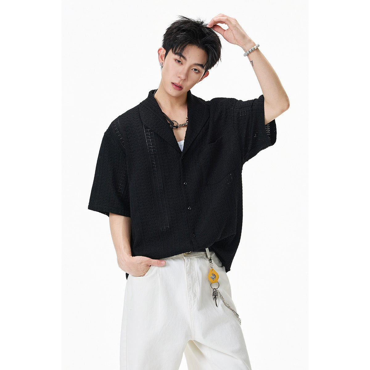 Close view of a model wearing a black short-sleeve textured button-up shirt with a notched collar and chest pocket.