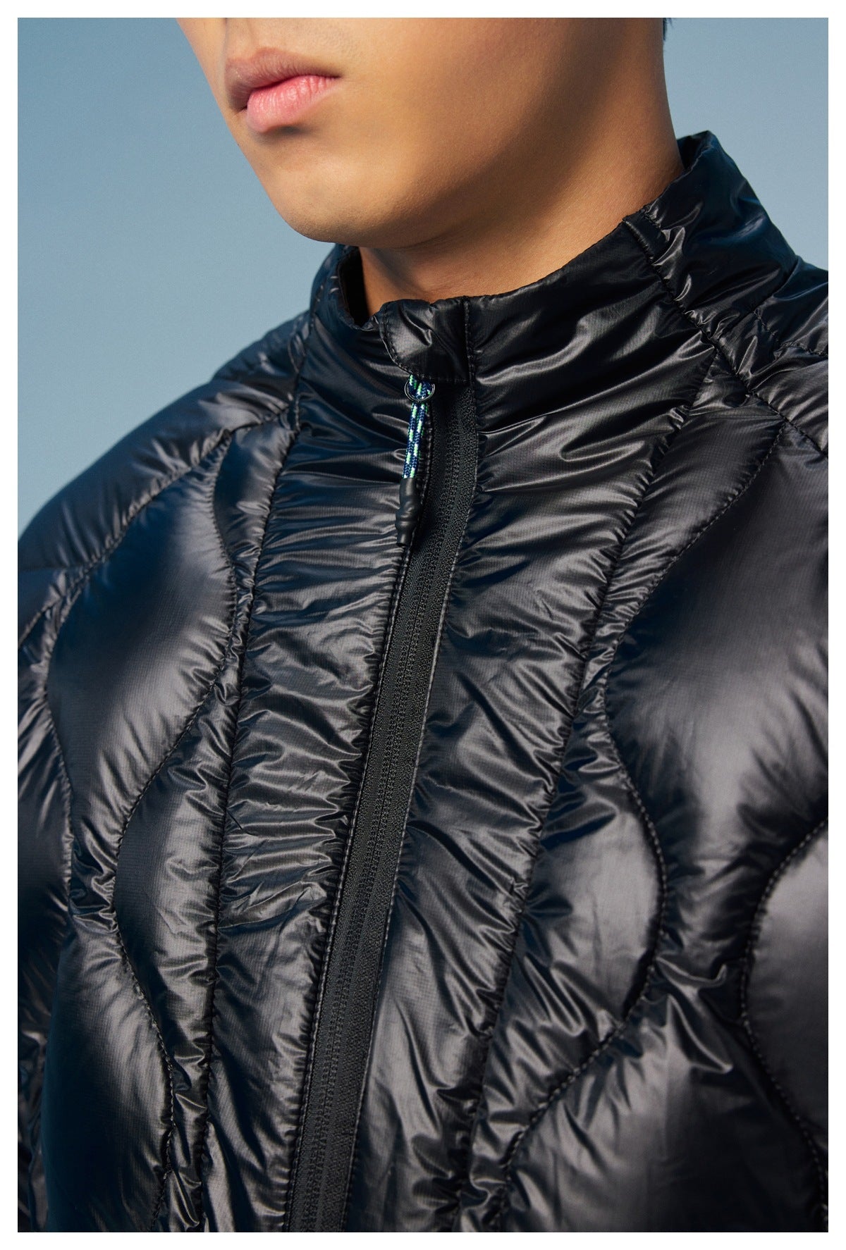 Close-up of the black quilted jacket's high collar, front zipper, patterned pull cord, and stitching.