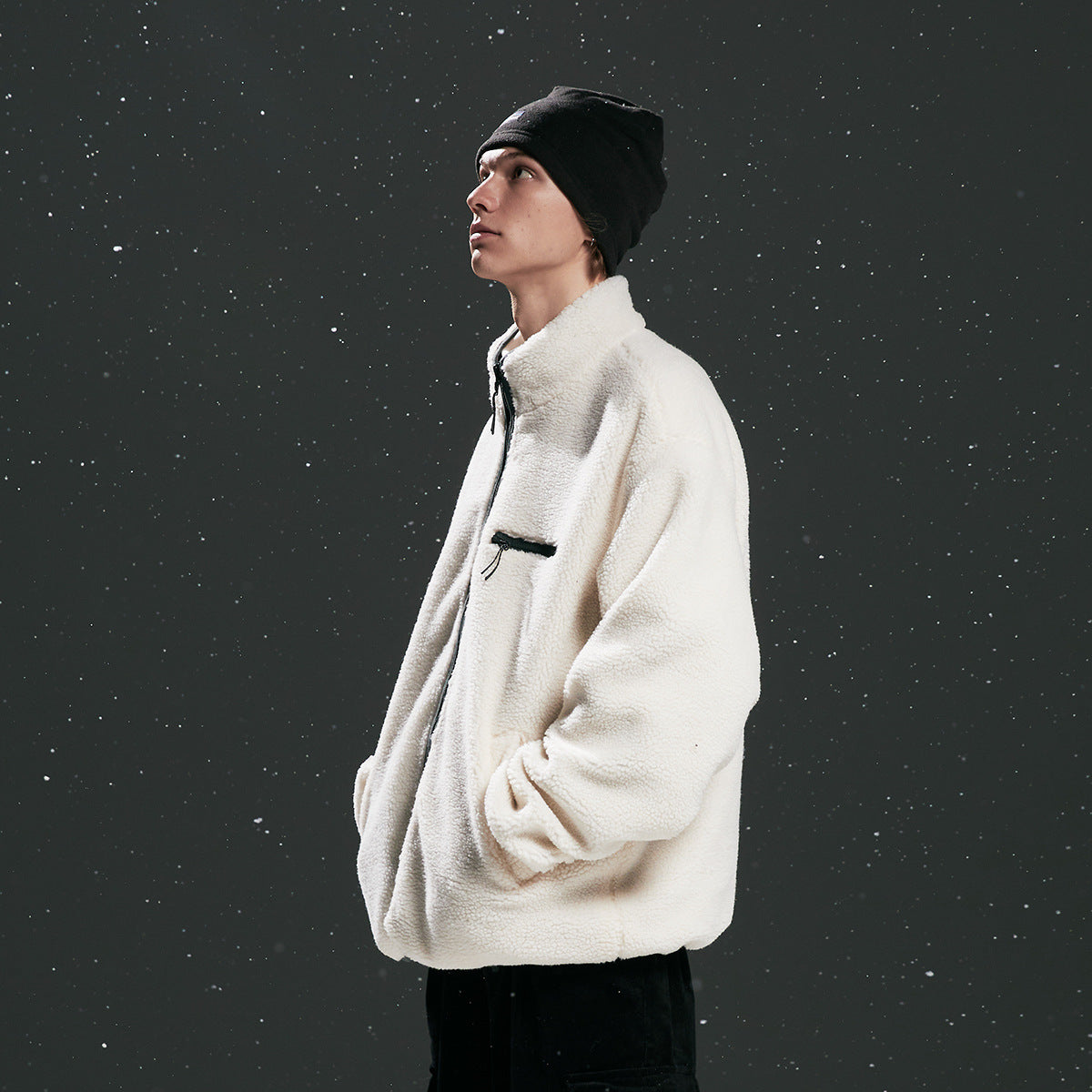 Side view of a model wearing an off-white fleece jacket with a chest zip pocket and black beanie.