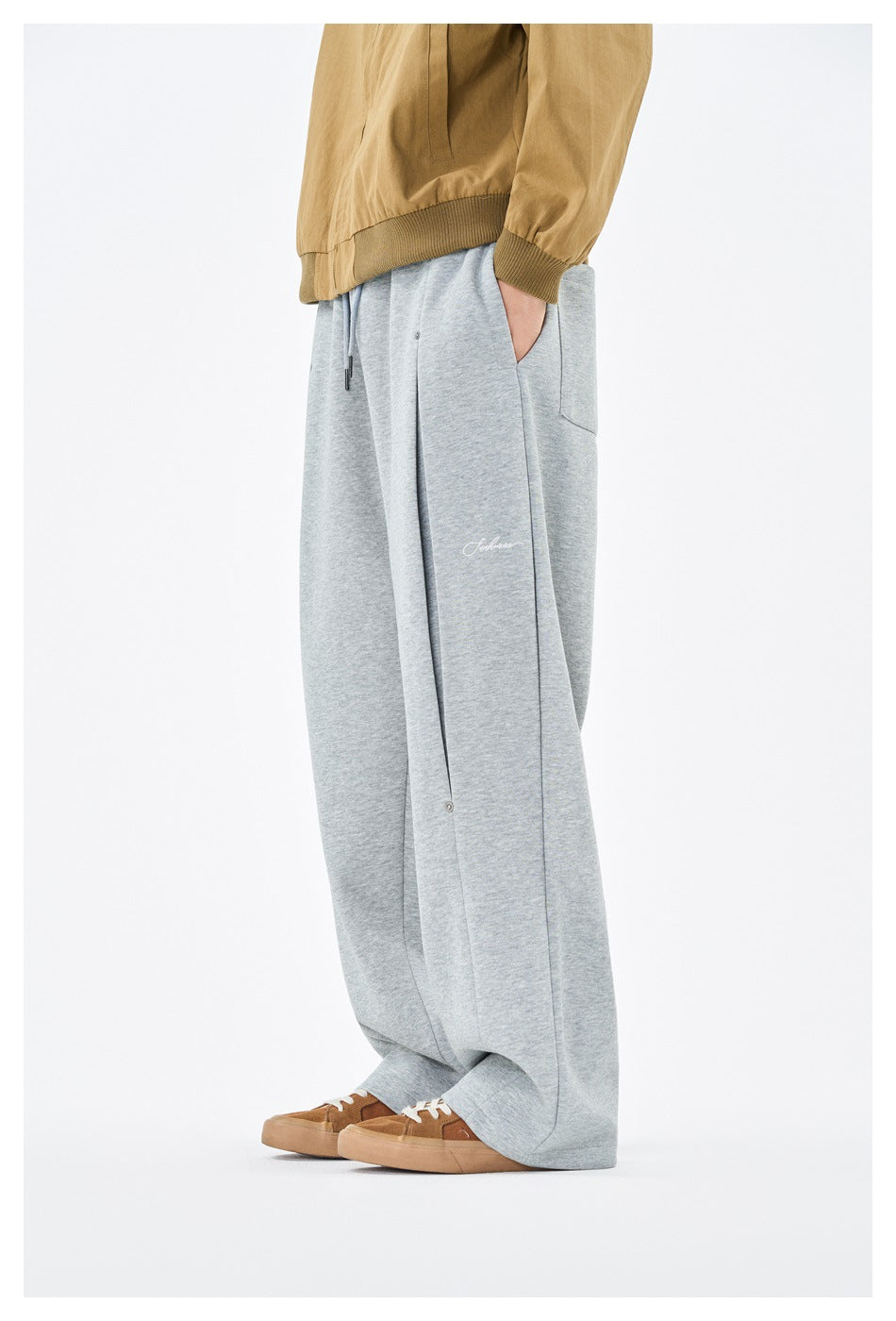 Side view of a person wearing heather gray wide-leg sweatpants with hand in pocket, tan jacket and brown sneakers