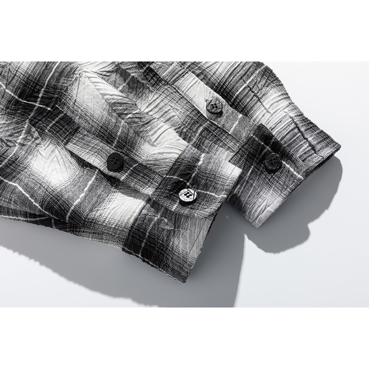 Close-up of the black, gray, and white plaid shirt sleeve cuff with several buttons.