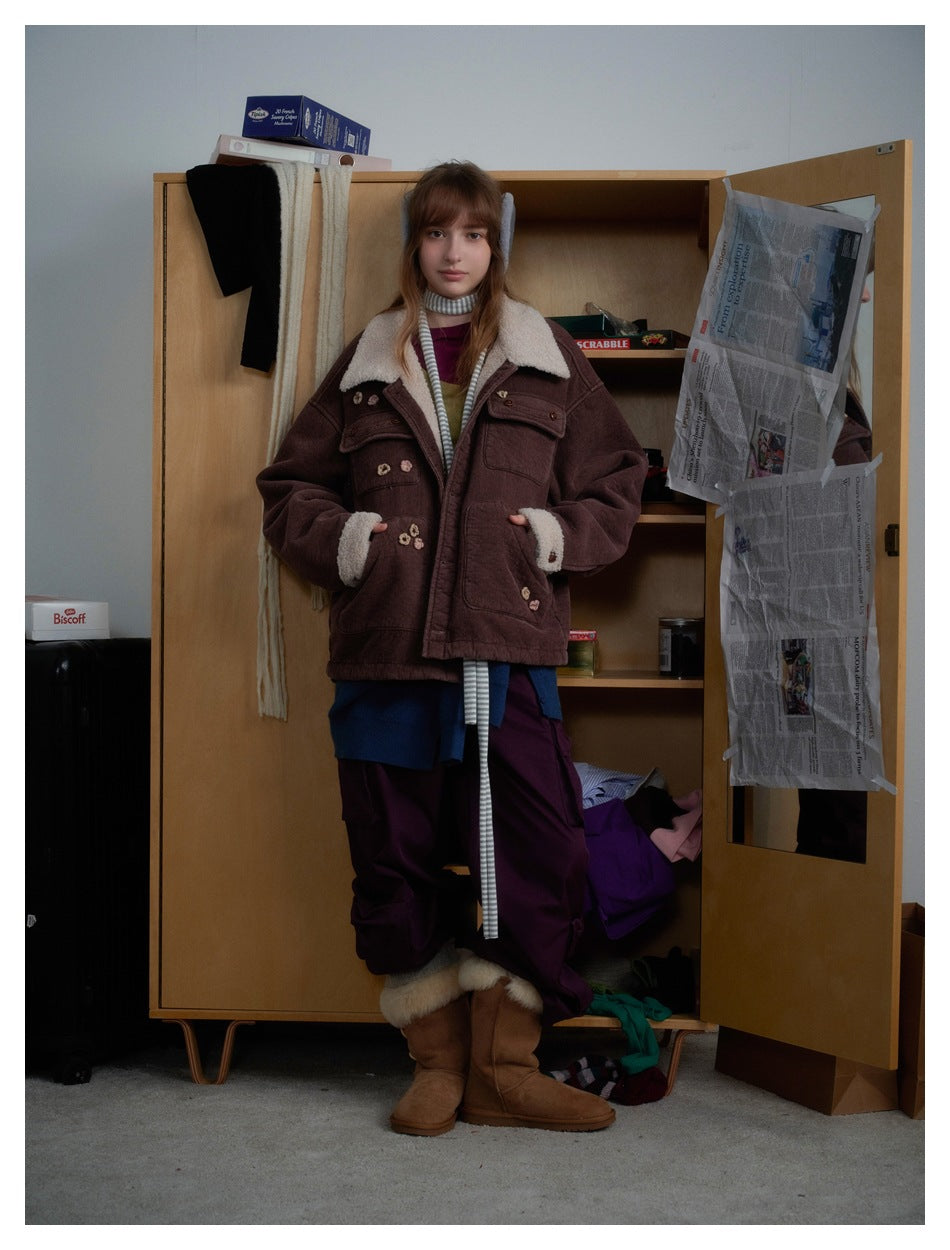 Model standing in a brown jacket with a cream collar and cuffs, floral details, and large front pockets.