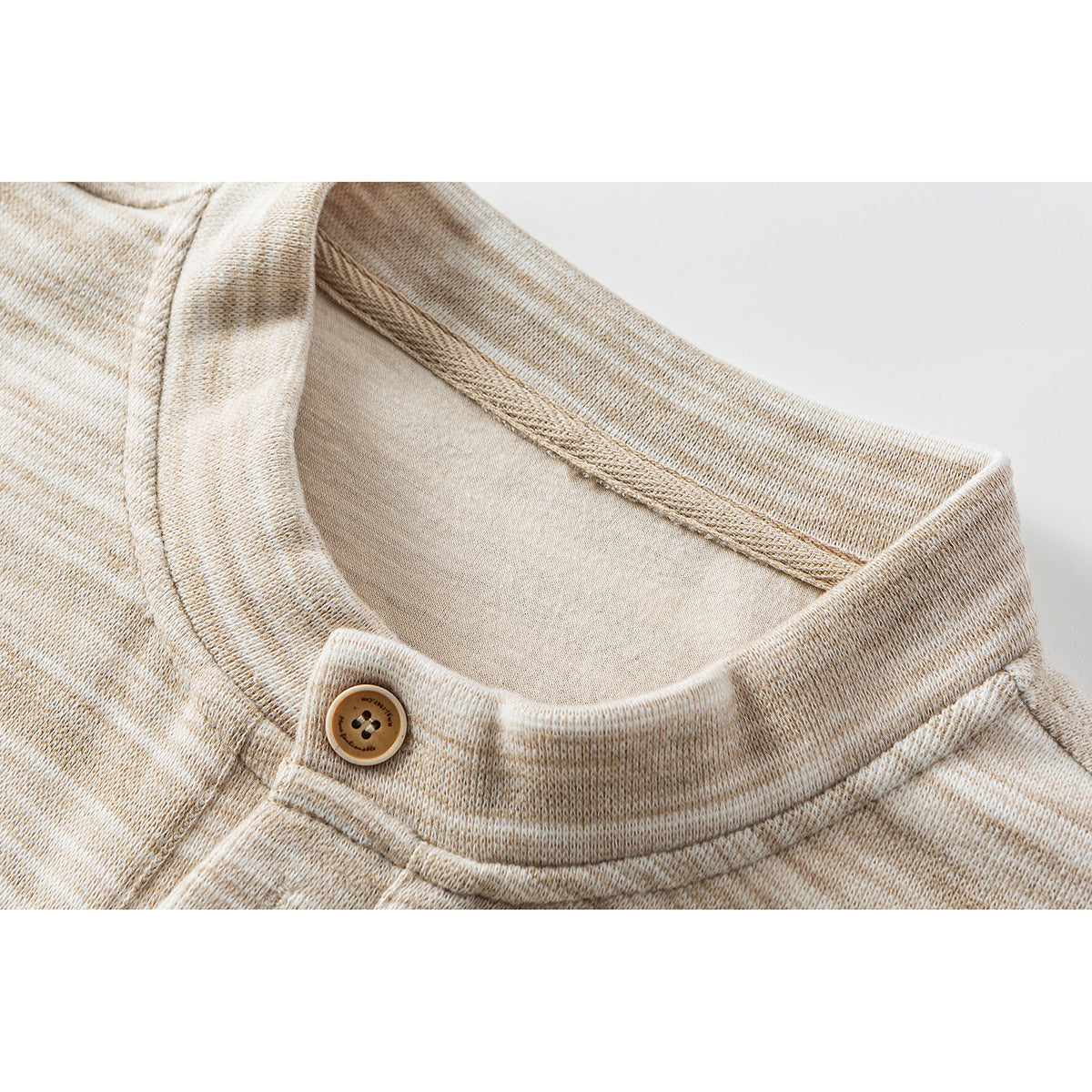 Close-up of a beige heathered shirt's band collar, button, and stitching.