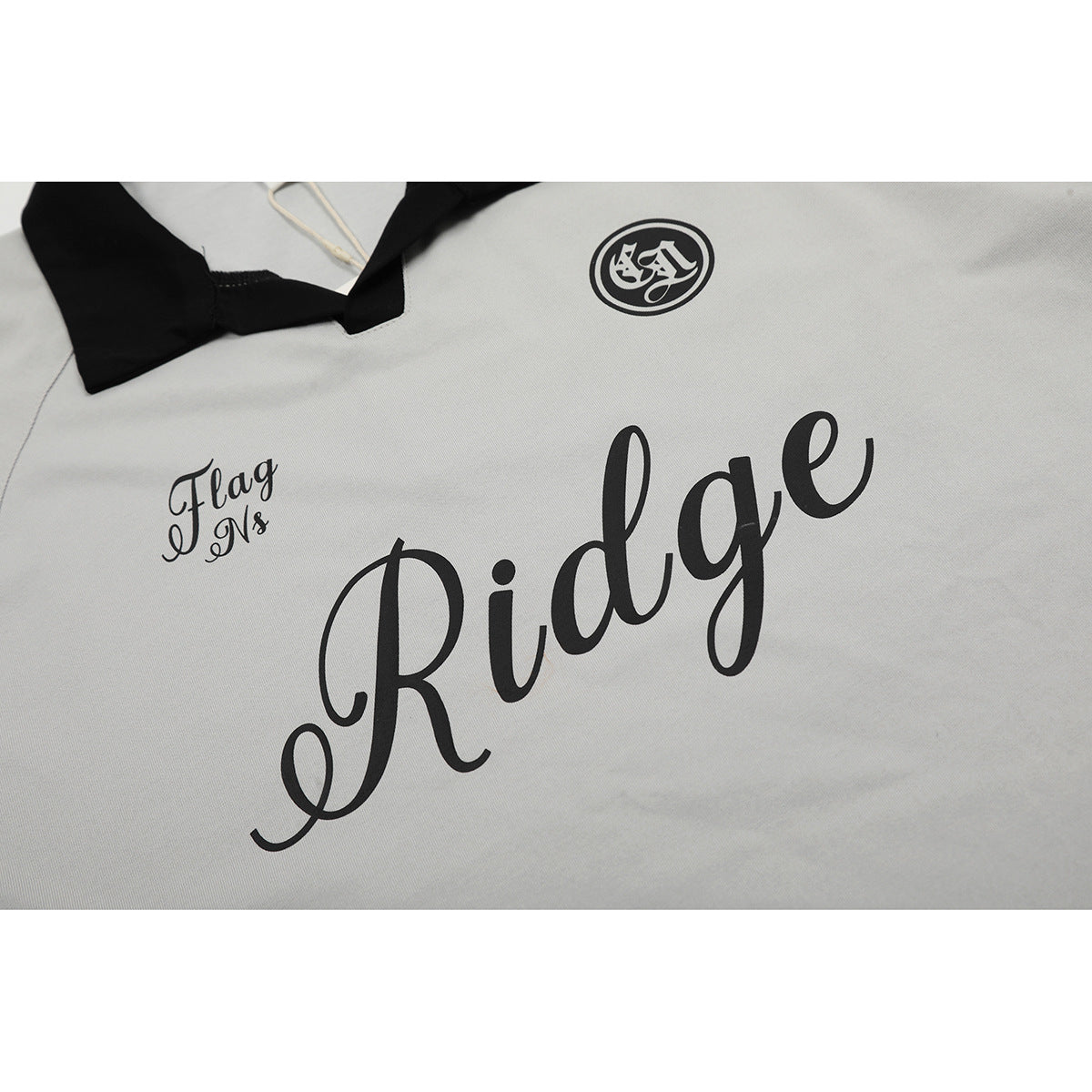 Close-up of a light gray polo shirt showing black script lettering and a small circular chest emblem.