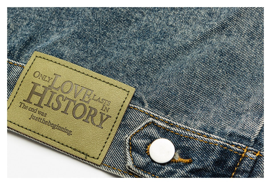 Blue denim waistband detail with a tan patch bearing English text and a white button.