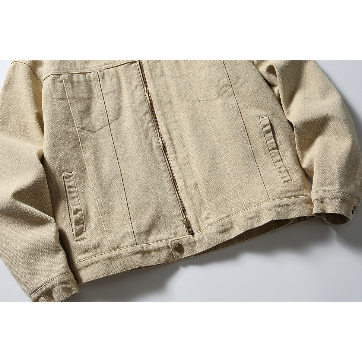 Cropped front view of a sand-colored jacket showing its zipper, front seams, angled pockets, cuffs, and hem.