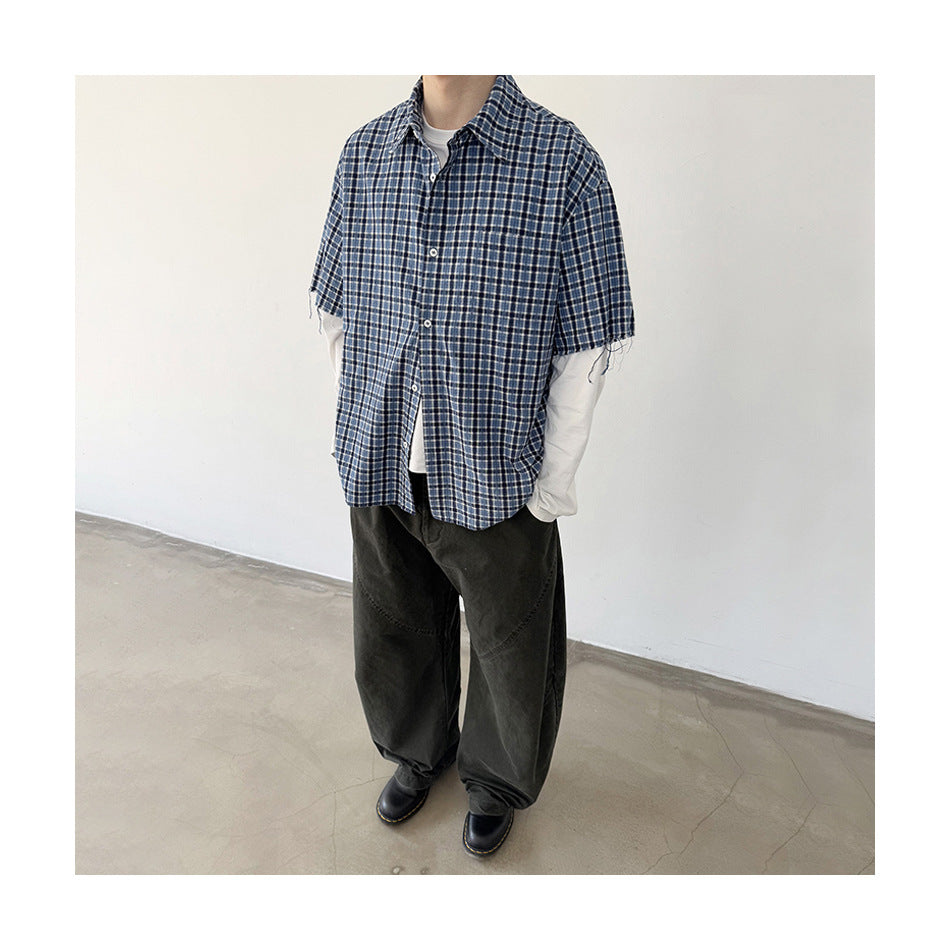 Cropped view of a model wearing a blue plaid short-sleeve button-up over a white long-sleeve shirt.