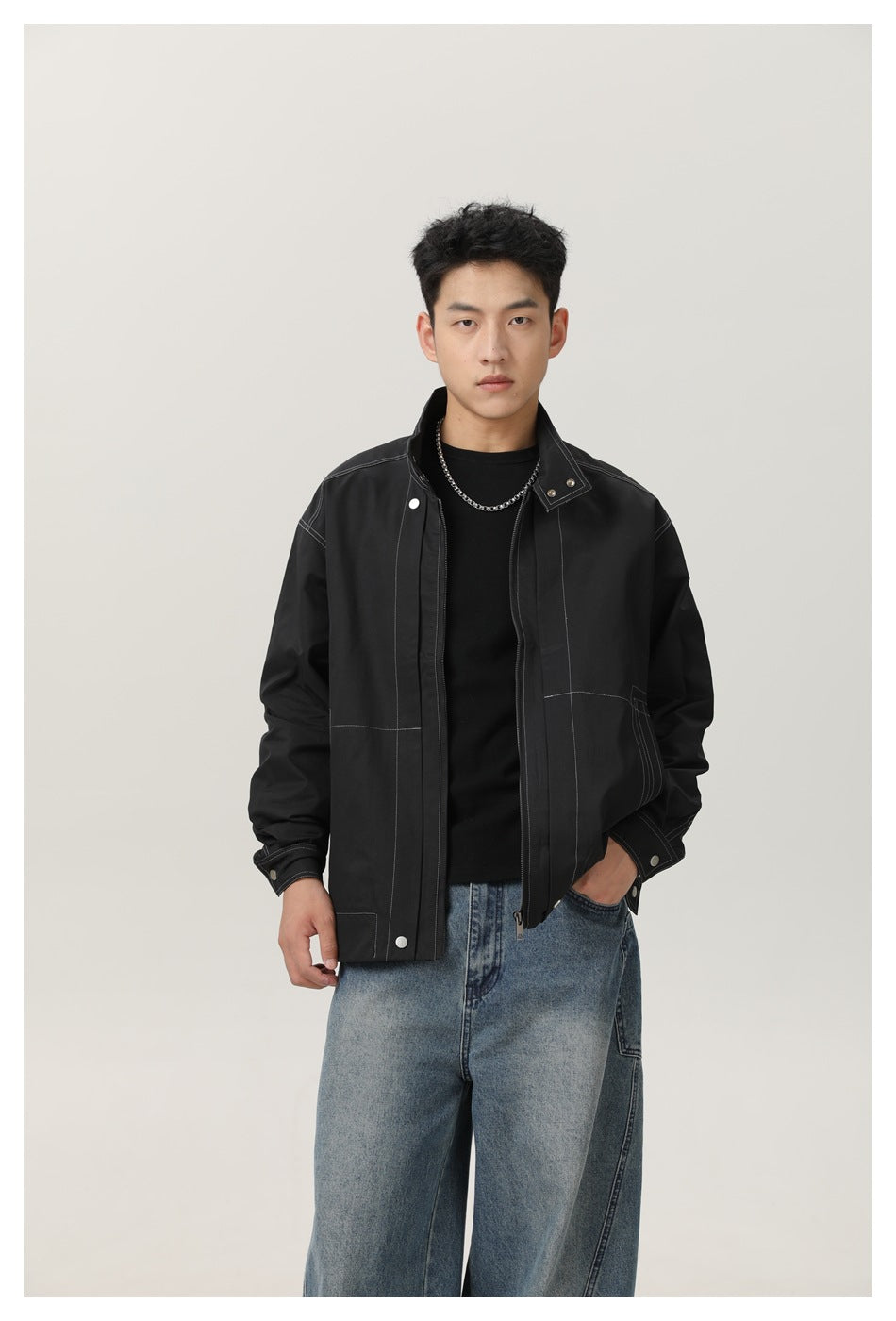 Front view of a model wearing a black contrast-stitched jacket over a black shirt.