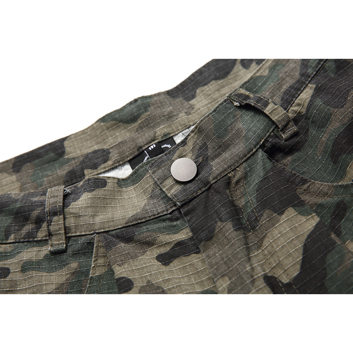 Close-up of olive, brown and black camouflage trousers showing the waistband, silver button, belt loop and fly seam.