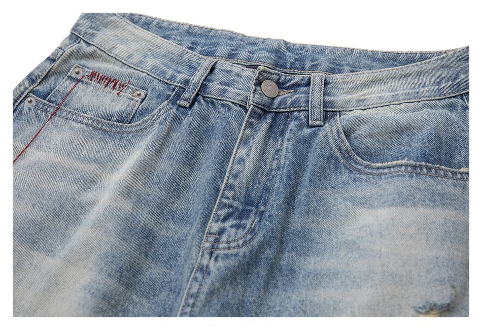 Cropped view of the front waistband and pockets of faded light-blue jeans with red stitching.