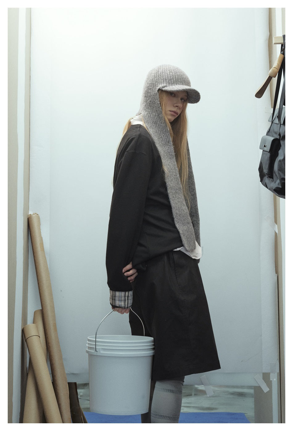 Model wearing a black sweatshirt with plaid cuffs, wide black shorts, and a gray knit cap with long side panels.