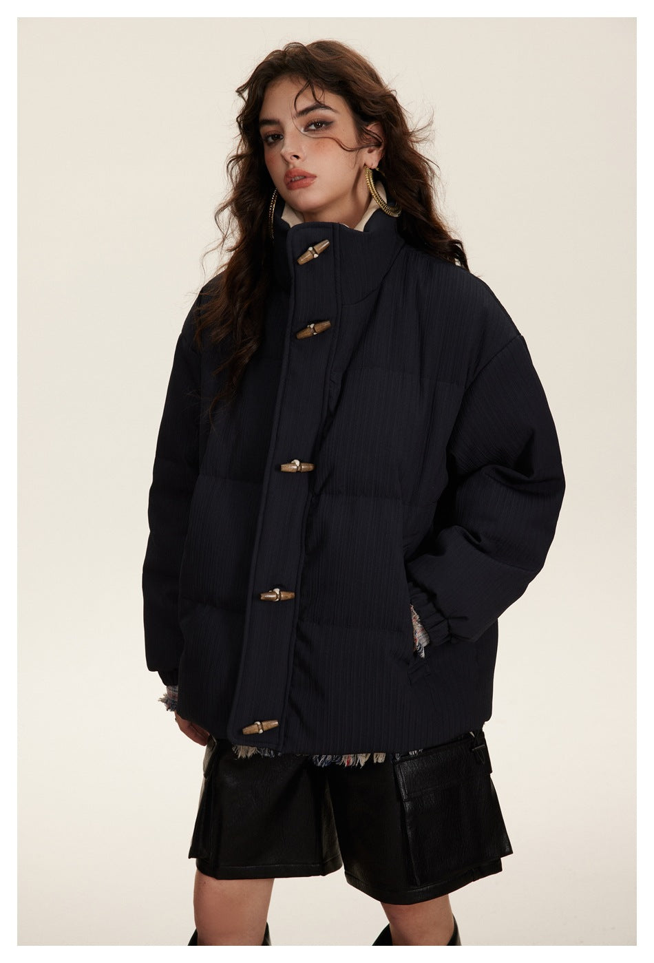Model wearing a dark navy padded toggle jacket with a high collar and black shorts, shown from the front.