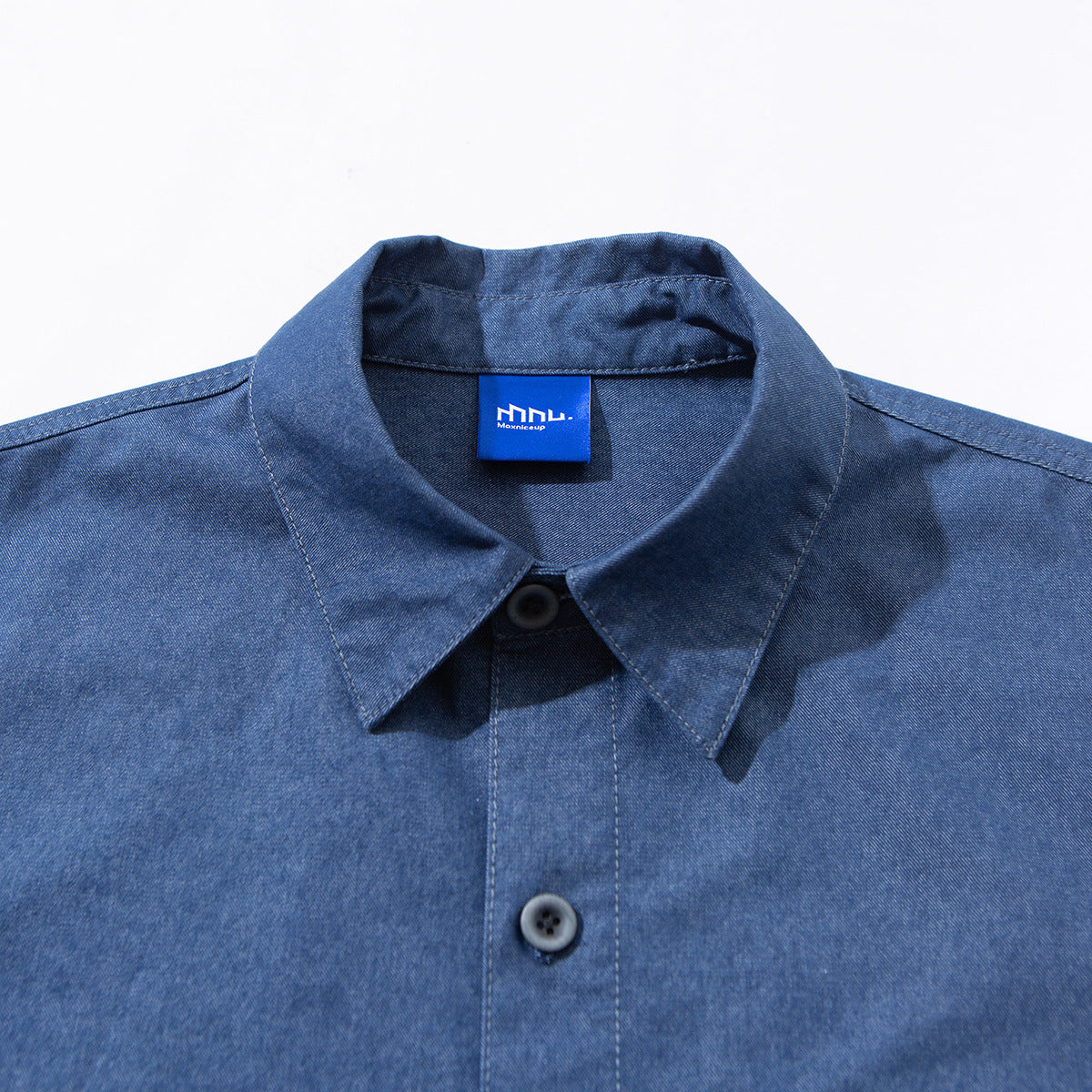 Close-up of a blue button-up shirt collar, placket and black buttons, with a blue neck label.