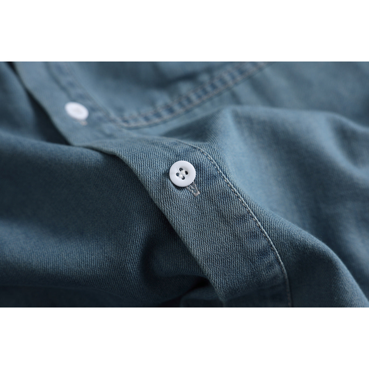 Close-up of a white button and stitched placket on blue denim fabric.